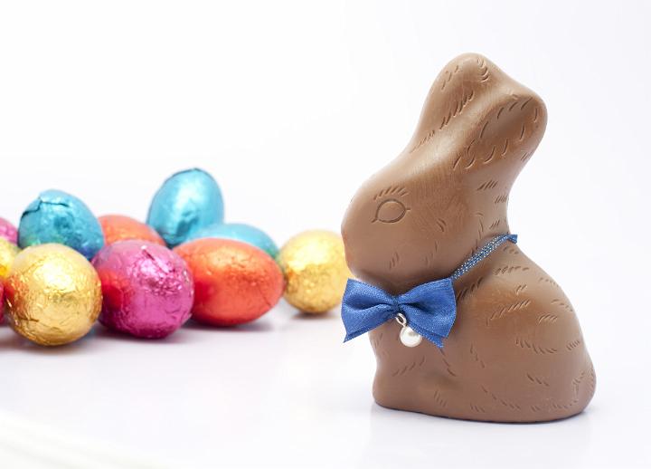 easter_bunny_eggs.jpg - Chocolate Easter bunny wearing a cute bow tie watching over a pile of colourful small Easter eggs