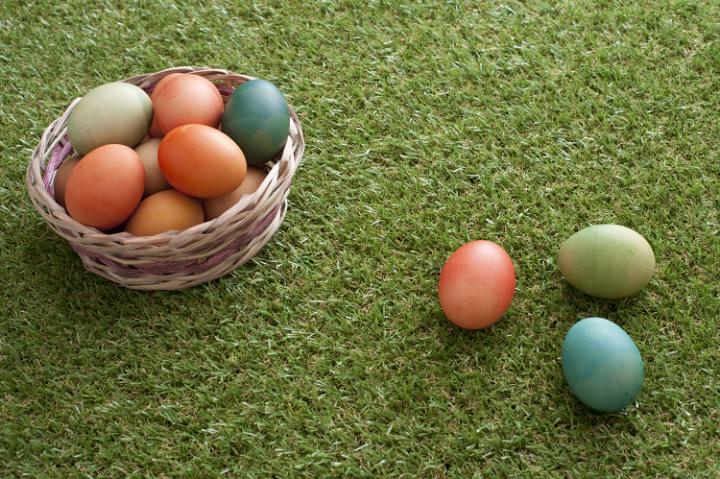 easter_egg_hunt.jpg - Tree painted eggs lying on green grass background next to Easter basket during egg hunt.