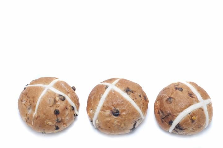 three_hot_cross_buns.jpg - Border of three freshly baked fruity spicy Hot Cross Buns on a white background with copy space for your seasonal greeting
