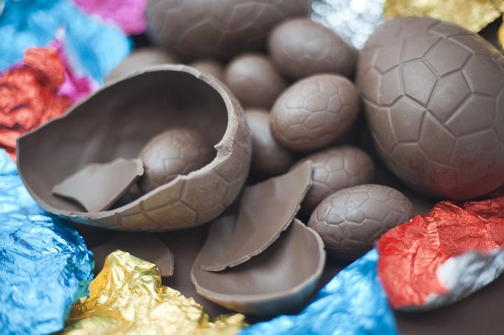 unwrapped_easter_eggs.jpg - Assortment of unwrapped chocolate Easter eggs lying amongst their colourful foil wrappers with an egg in the foreground broken into pieces