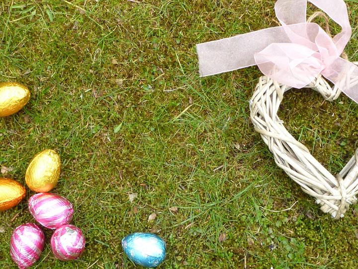 easter_love_background.jpg - Close-up background for Easter with colorful chocolate eggs and wicker heart decorated with pink ribbon, viewed from above with copy space