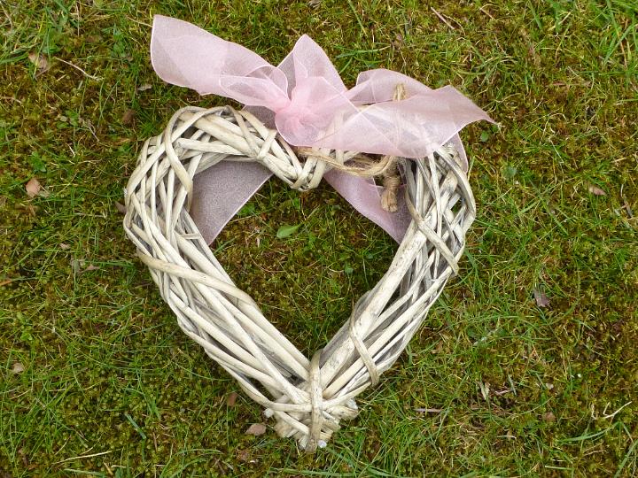 easter_theme_background.jpg - Wicker heart with pink ribbon on fresh green grass in spring, viewed from above in full frame Easter theme background