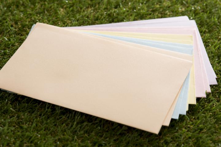 envelopes.jpg - Assorted stack of blank pastel colored envelopes fanned out over a green lawn in a close up high angle view