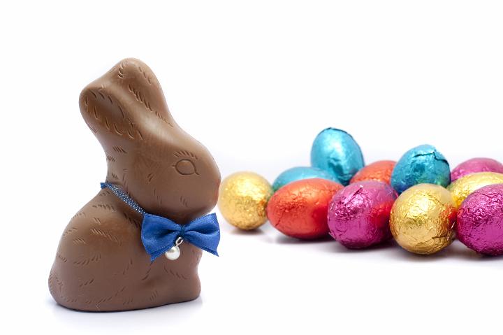 easter_rabbit_and_eggs.jpg - Sideways view of a chocolate Easter Rabbit wearing a bowtie together with a pile of colourful foil wrapped eggs on white