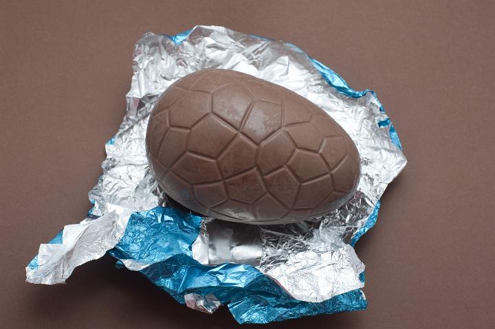chocolate_egg.jpg - Single unwrapped chocolate Easter Egg sitting on its colourful shiny silver and blue foil wrapper on a brown background