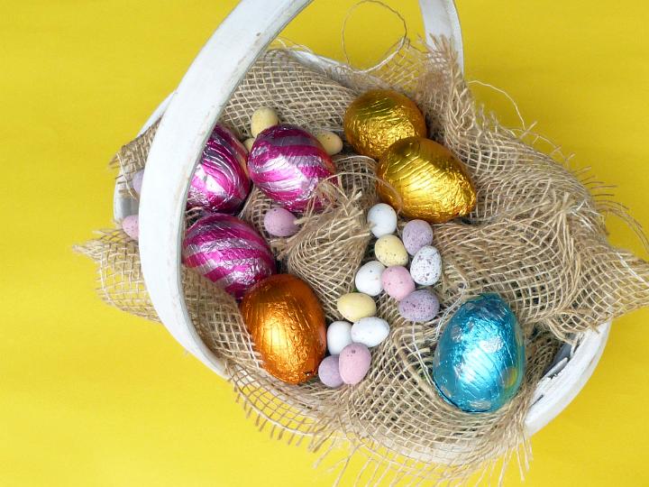 collected_eggs.jpg - Rustic decorative Easter basket with colorful eggs nestling on hessian over a yellow background
