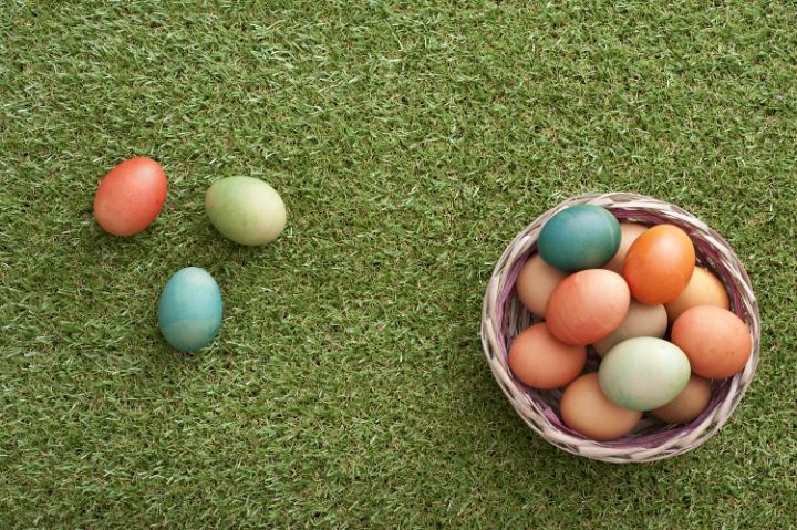 easter_eggs_hunt.jpg - Overhead view of three colorful Easter eggs in grass beside woven basket filled with more of them