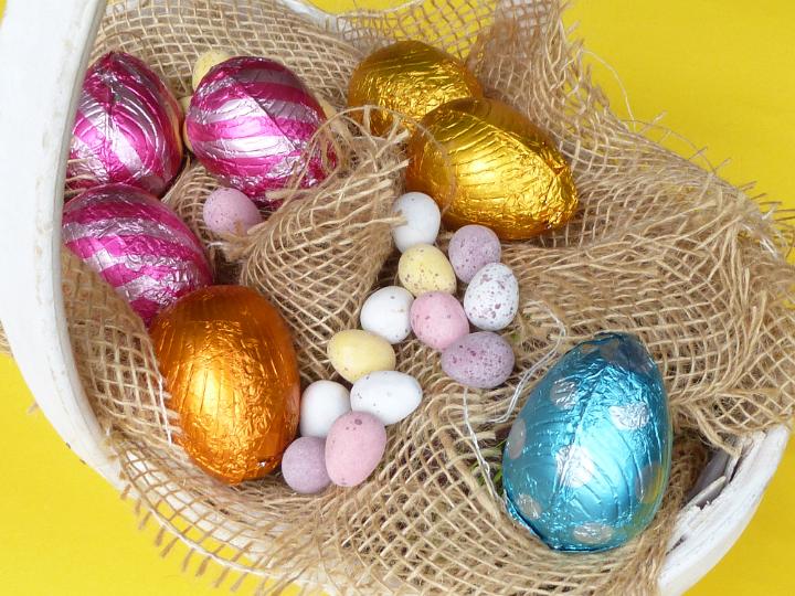 egg_basket_for_easter.jpg - Collected Easter eggs from the egg hunt in a basket with assorted sugar-coated and foil wrapped chocolate candy on a bed of hessian viewed top down