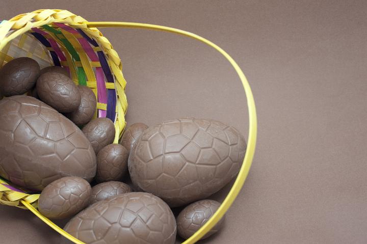 milk_chocolate_eggs.jpg - Milk chocolate Easter Eggs spilling out of a basket onto a brown background with copyspace