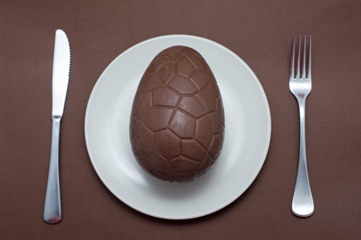 easter_egg_concept.jpg - Place setting with a chocolate Easter egg served for dinner on a plate with cutlery over a matching brown background