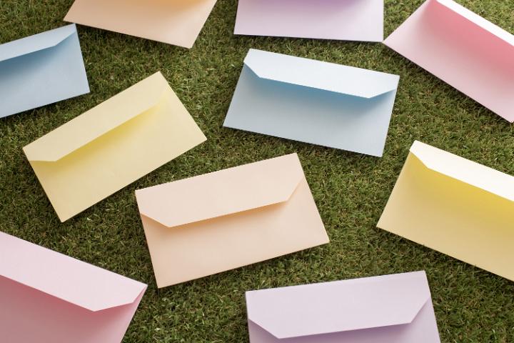 easter_greetings.jpg - Scattered colorful pastel envelopes lying on fresh green grass in a concept of spring and Easter greetings and messages, overhead view in a full frame background