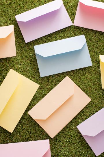 easter_wishes.jpg - Scattered pastel colored envelopes on green grass in a concept of Easter wishes and greetings in an overhead full frame background view